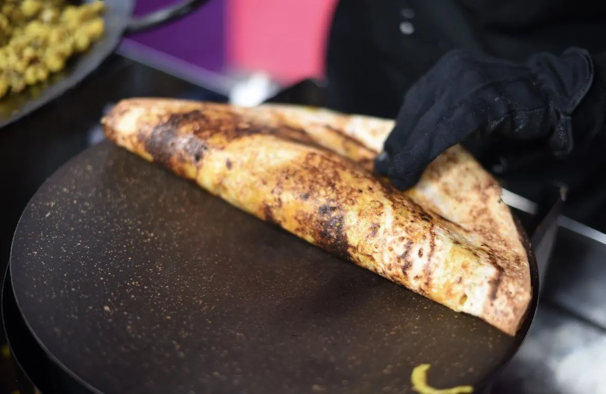 A finished dosa being folded on the tawa, golden and crisp
